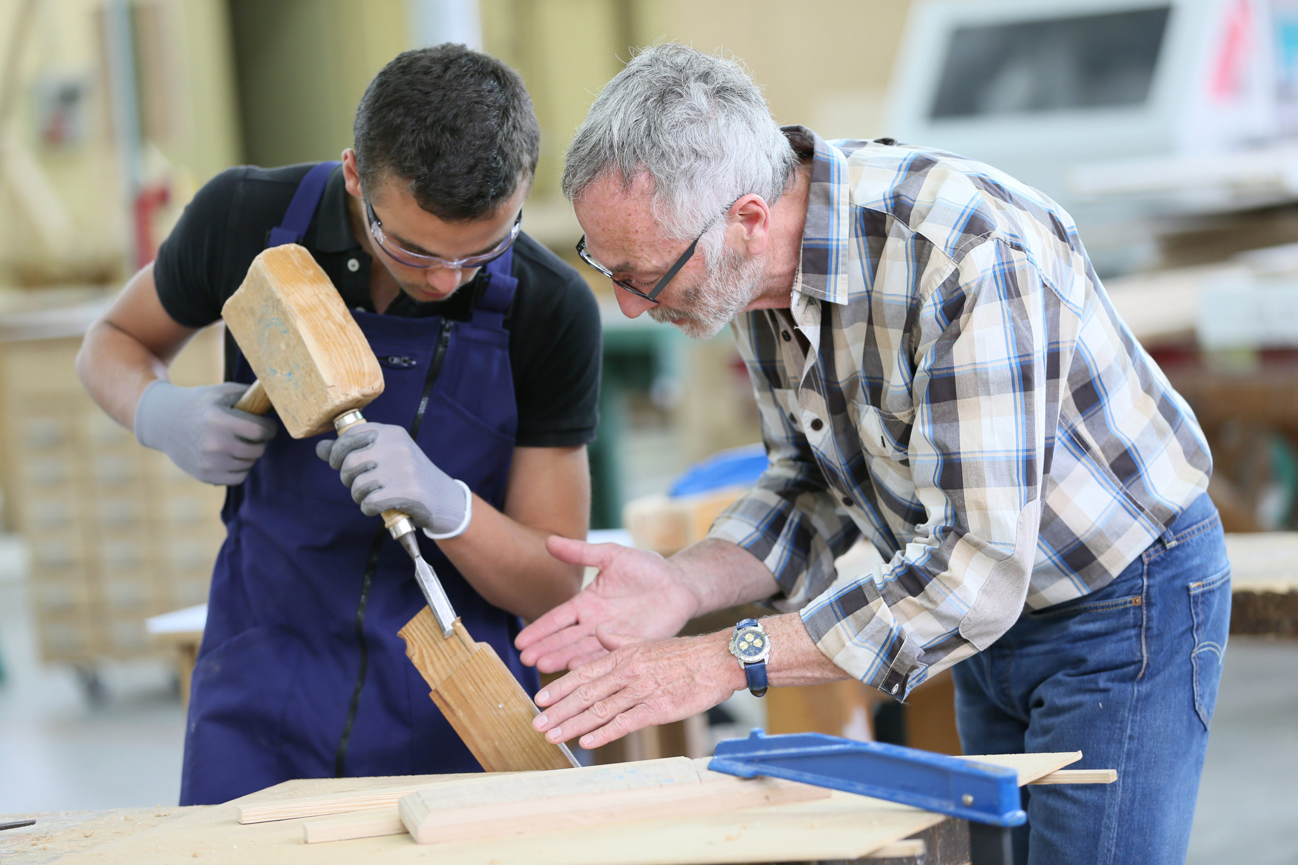 Young,Apprentice,With,Teacher,Working,On,Piece,Of,Wood Photo d'un artisan encadrant un jeune lors d'un chantier participatif